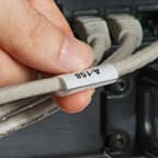 Une personne tenant une étiquette à enrouler appliquée sur un câble gris.