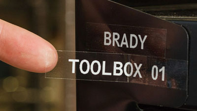 Une étiquette transparente, contenant le texte blanc « Brady toolbox 01 », appliquée sur une pièce métallique.