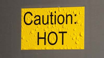 Une étiquette Brady ToughWash jaune sur laquelle est imprimé le texte « CAUTION HOT ». L’étiquette est humide, comme si elle avait été récemment nettoyée par pulvérisation.