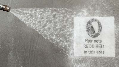 Un employé utilise un jet d’eau pour nettoyer une étiquette à métaux détectables Brady ToughWash, appliquée sur une machine.