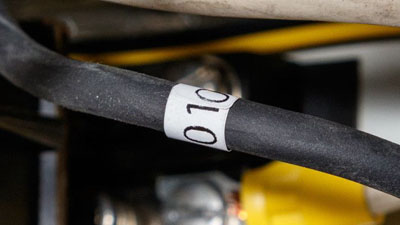 Une étiquette en Tedlar blanc auto-extinguible à enrouler contenant un texte noir appliquée autour d’un fil noir d’une boîte électrique.